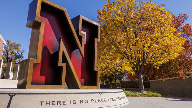 Large red and black letter "N" monument with vibrant autumn trees and blue sky.